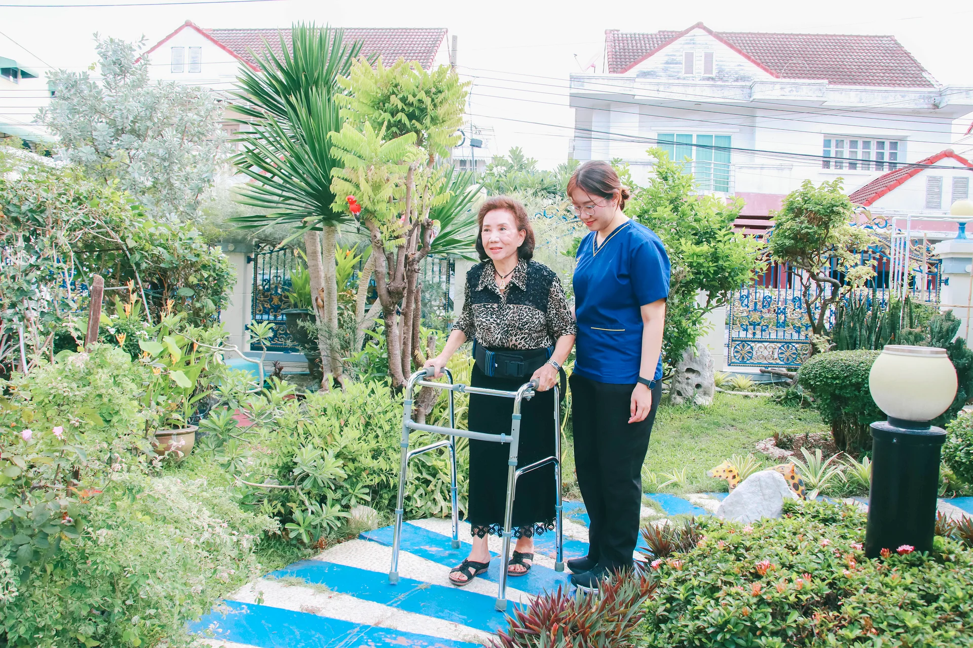 KIN physical therapist practising walker gait with an older adult on uneven surfaces in the patient&rsquo;s garden