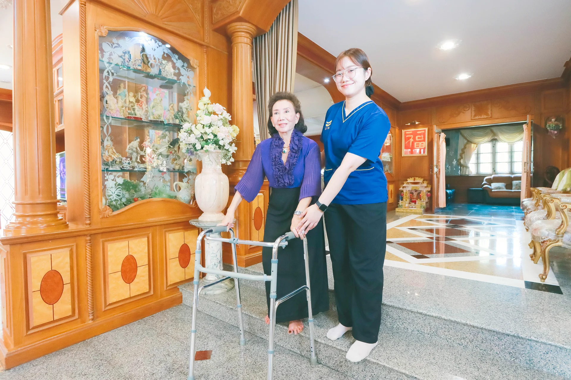 Full-body view of a KIN physical therapist helping a stroke patient practise walking with a walker at home